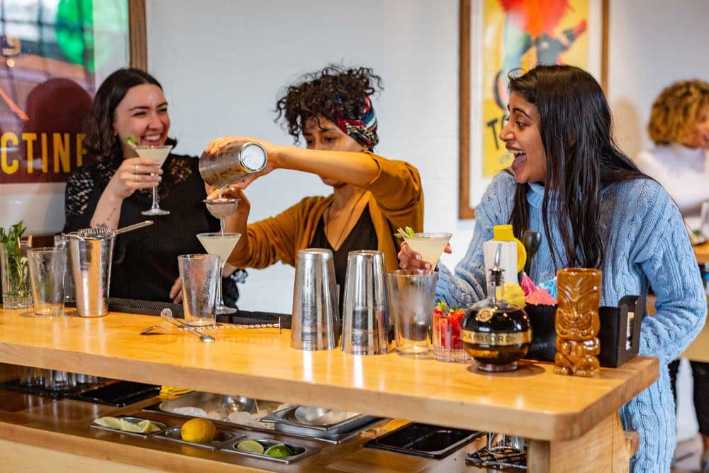 Three women at a micro bar making cocktails while lauging