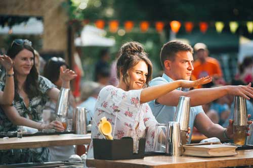 Man and women tapping the top of a cocktail shaker in an outdoor class