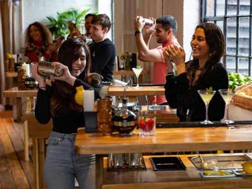 Two women take part in a public cocktail making class in Shoreditch, with others in background
